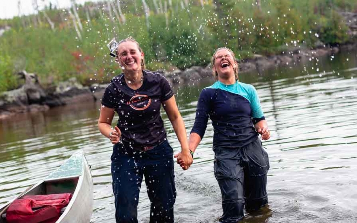 two people standing knee-deep in water hold hands and laugh after being splashed